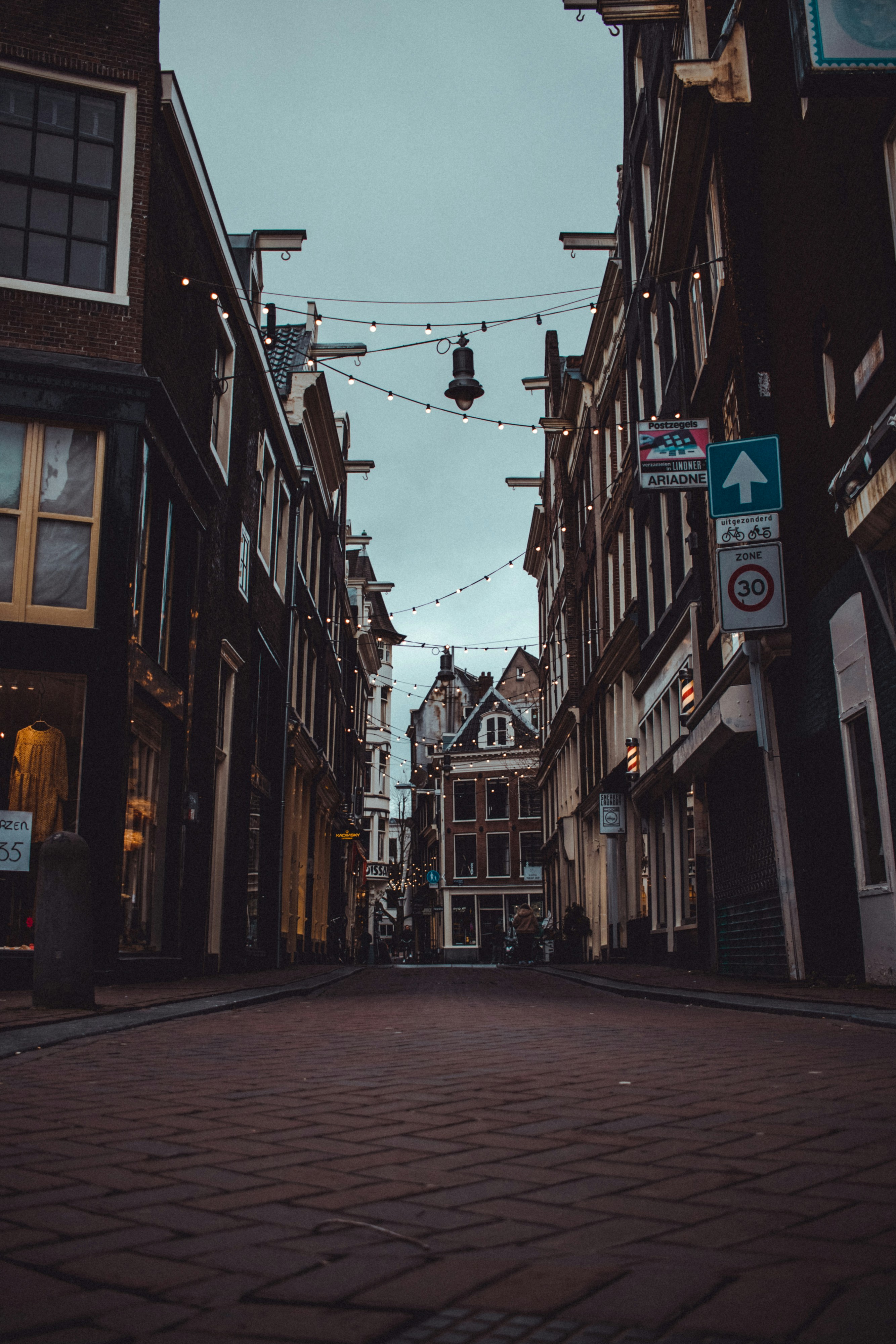 A cobbled street at night with lights strung overhead, between the buildings